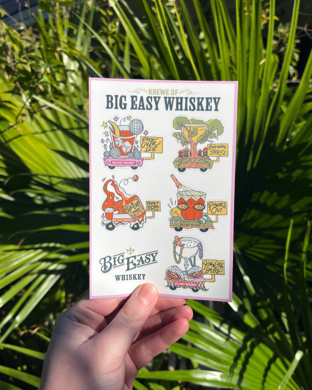 Sticker Sheet with Big Easy Whiskey graphics held in front of green foliage